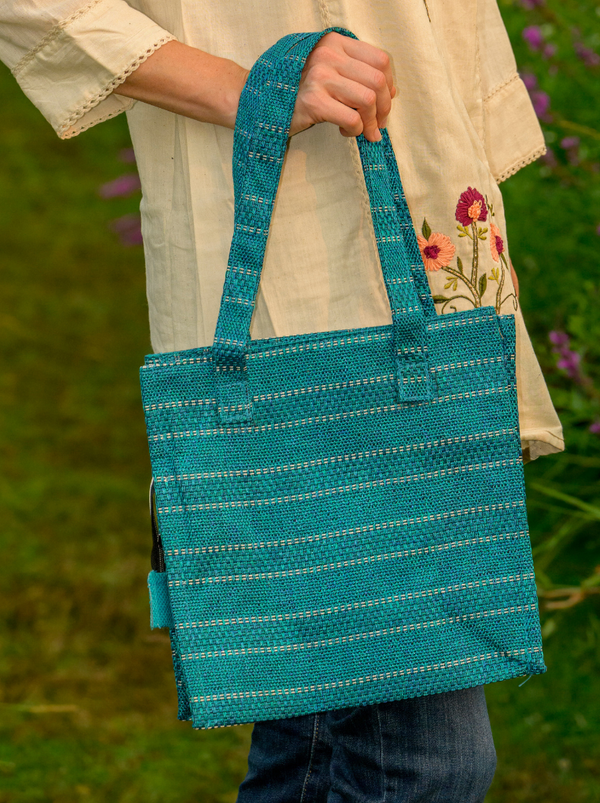 Person holding a blue woven tote bag against a blurred green background