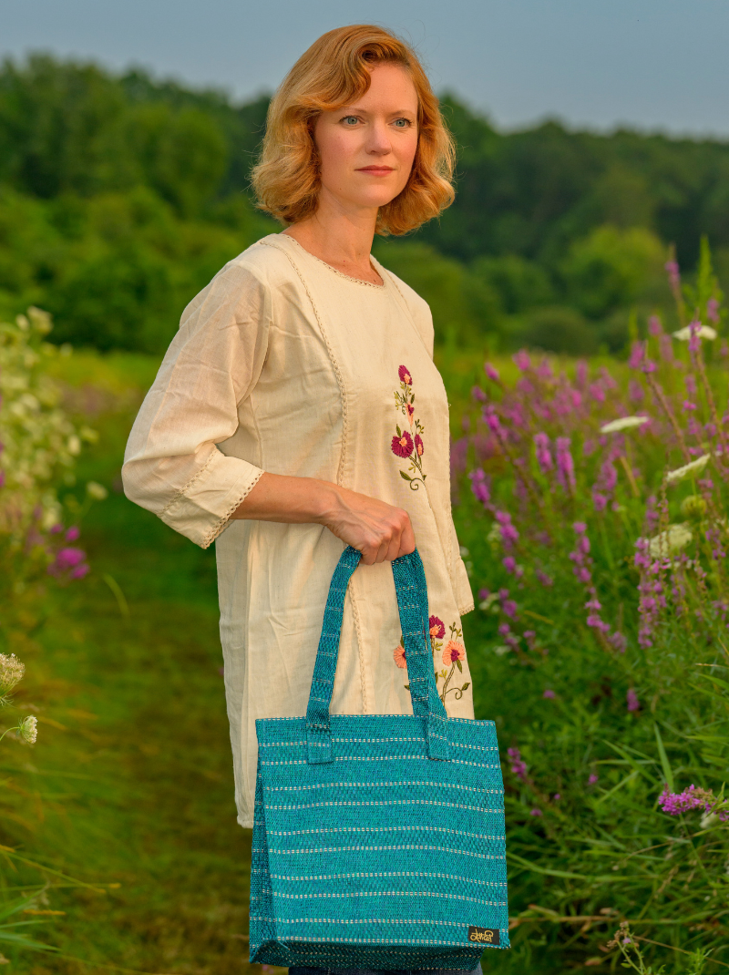 Woman holding a blue bag in a field with greenery and flowers