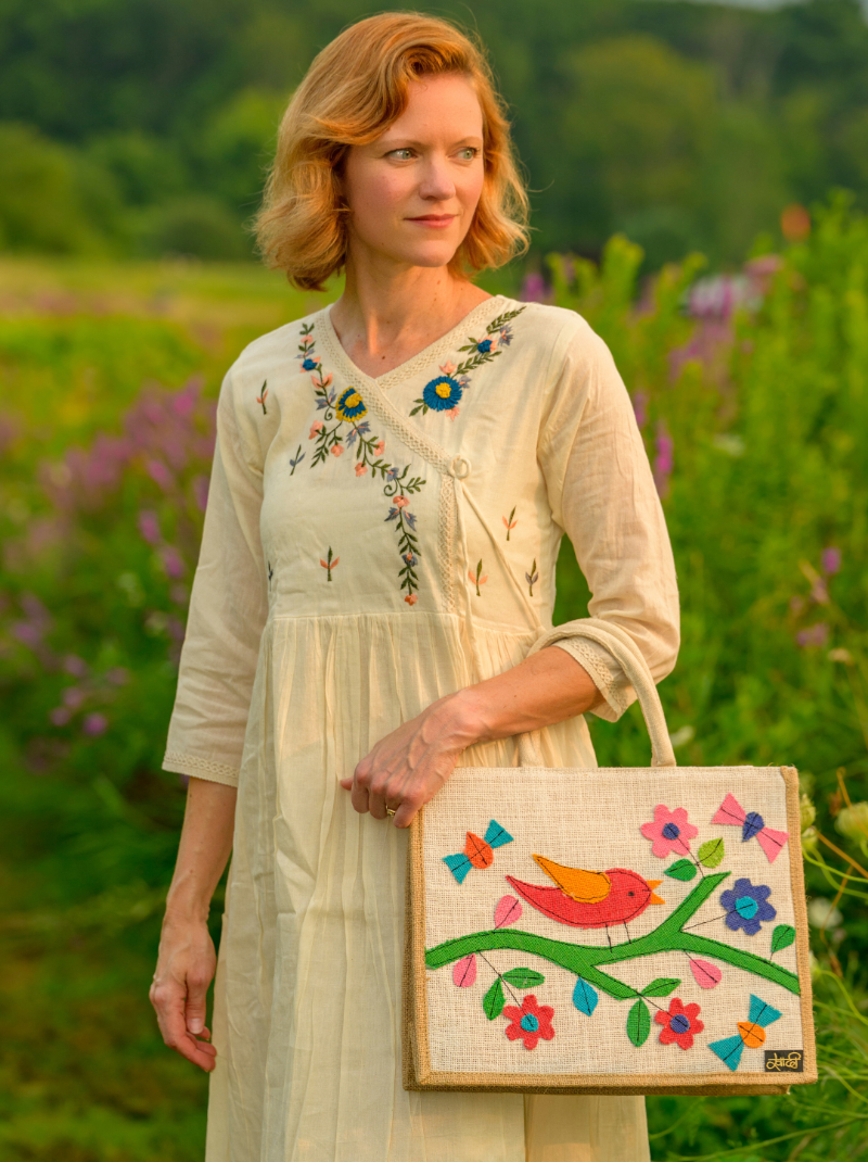 Woman holding a colorful embroidered bag in a field