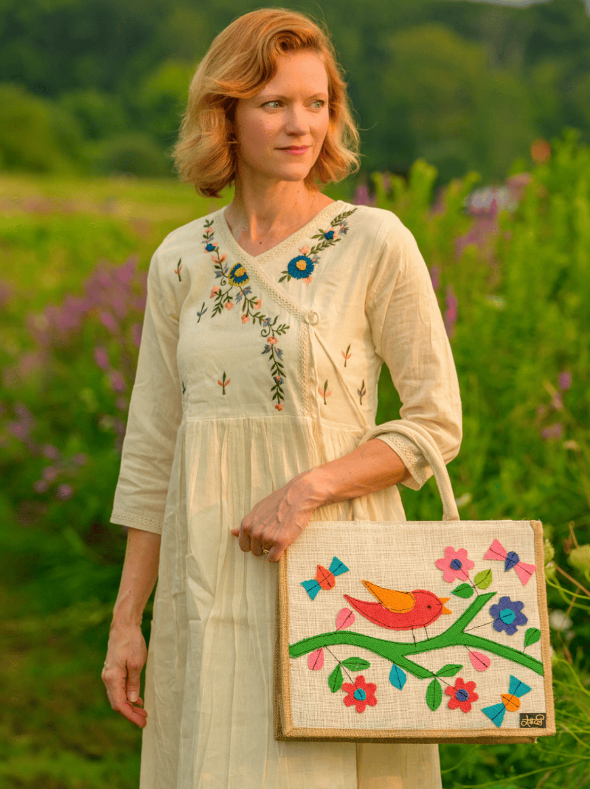 Woman holding a colorful embroidered bag in a field