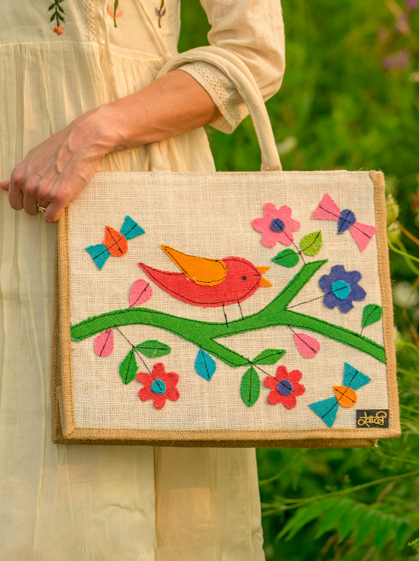Handbag with colorful bird and floral design held by a person in a natural setting