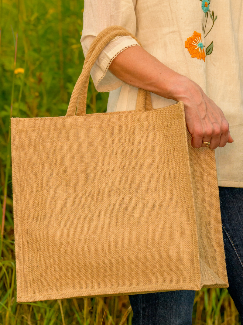 Person holding a beige jute bag in a natural setting