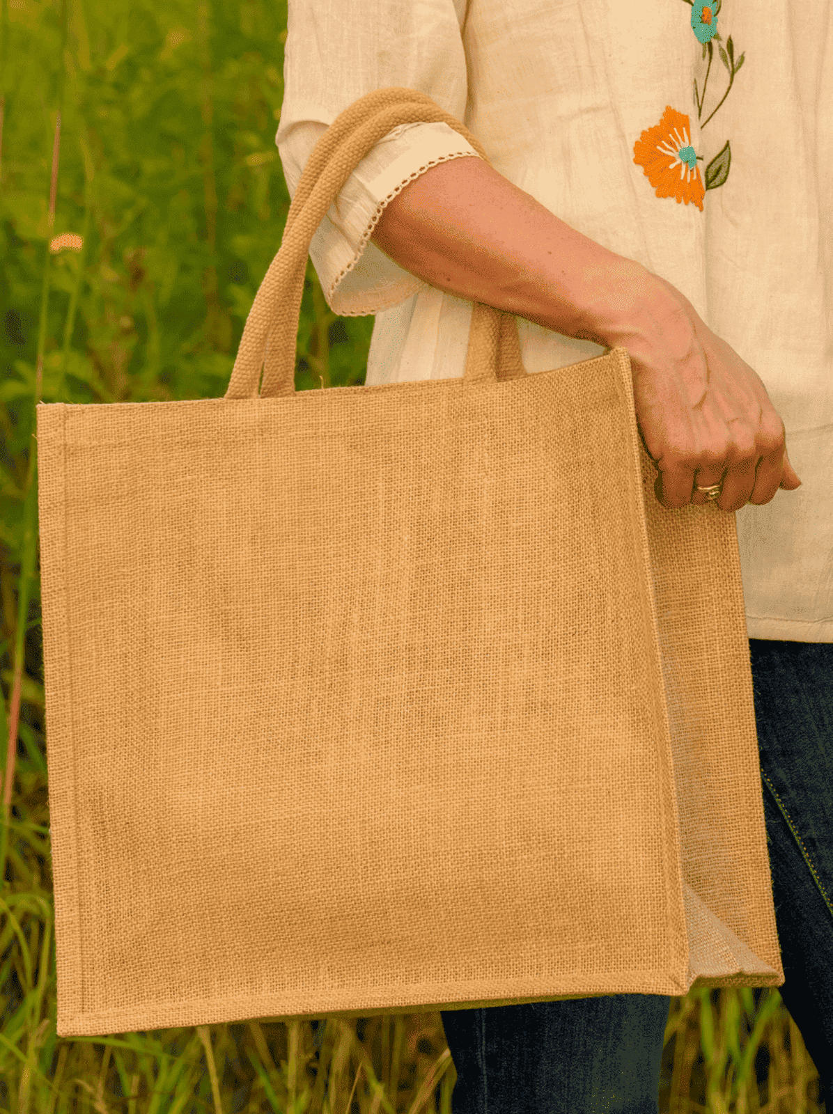Person holding a beige jute bag in a natural setting