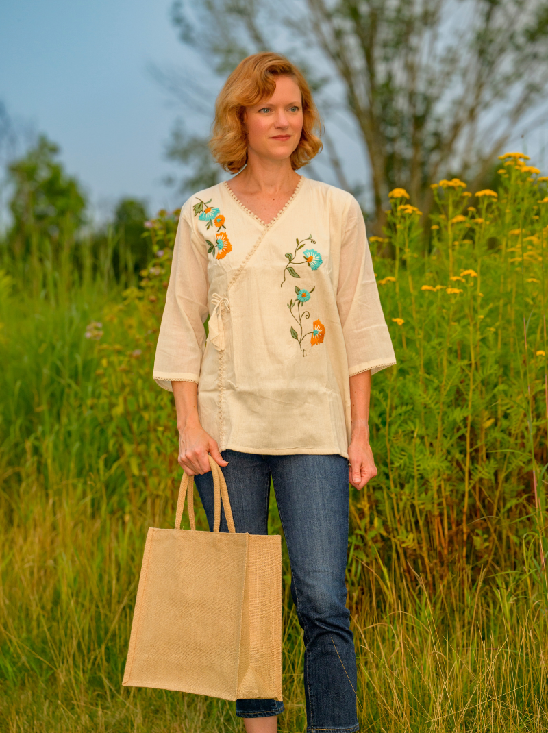 Woman holding a beige tote bag in a field with embroidered top