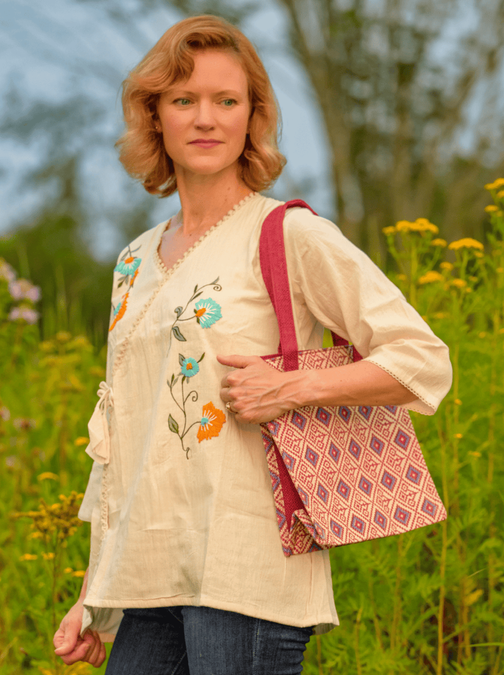 Woman holding a patterned bag in a field with flowers