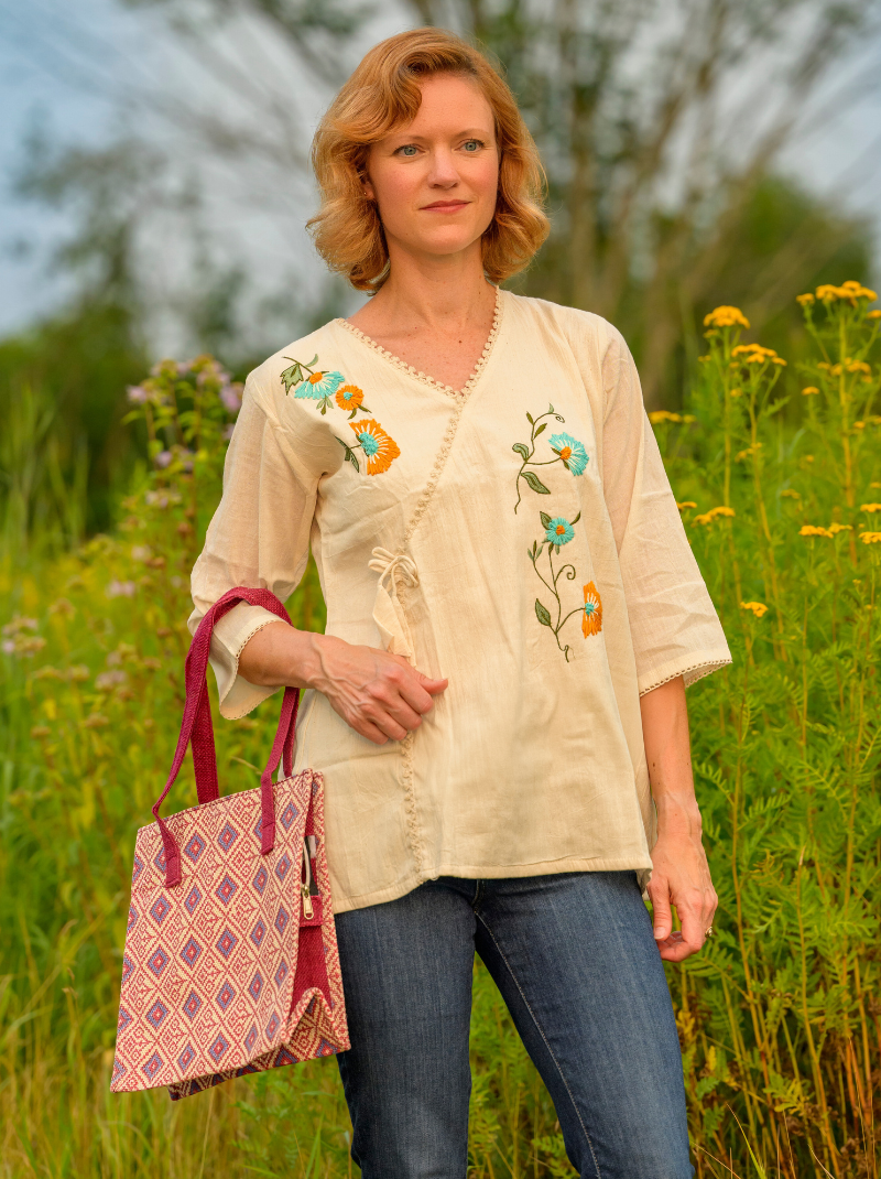 Woman in a beige embroidered blouse standing in a field with flowers