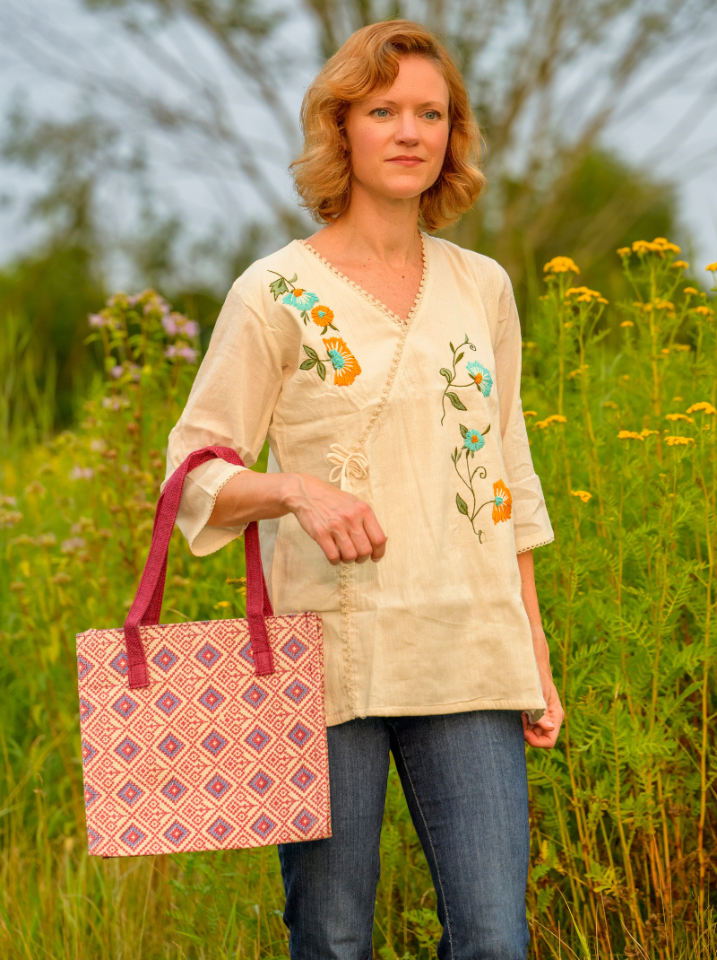 Woman holding a patterned bag in a field with embroidered top