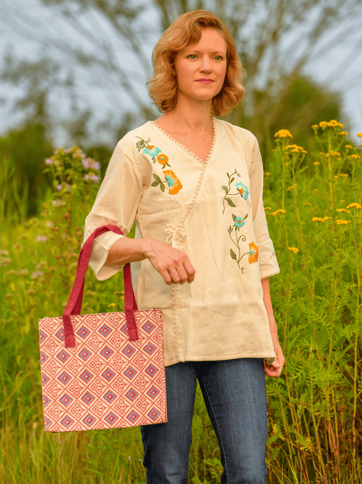 Woman holding a patterned bag in a field with embroidered top