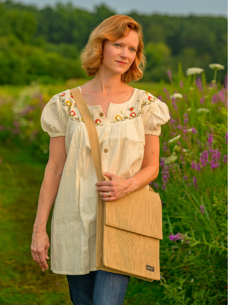 Woman in a floral blouse holding a beige bag in a field with flowers