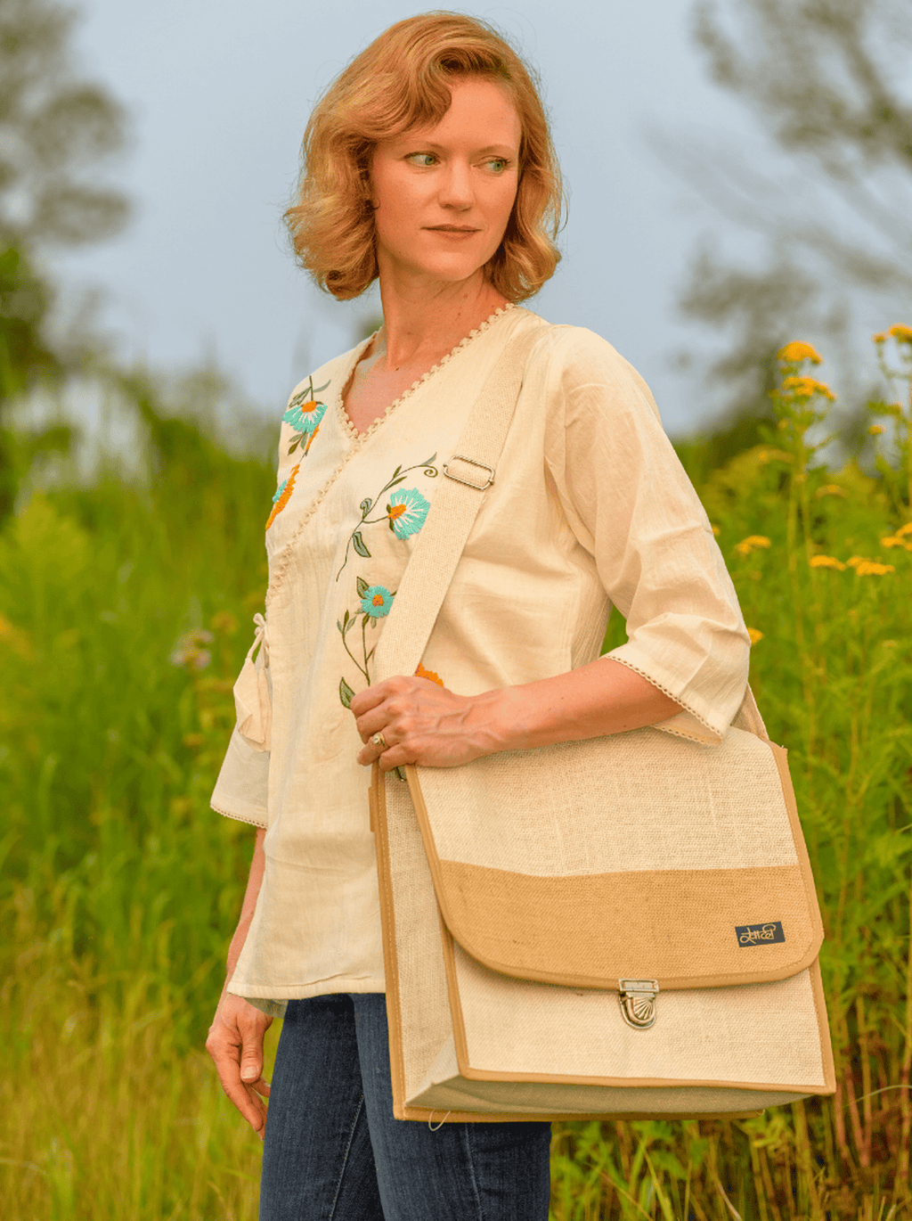 Woman holding a beige bag with floral embroidery in a field