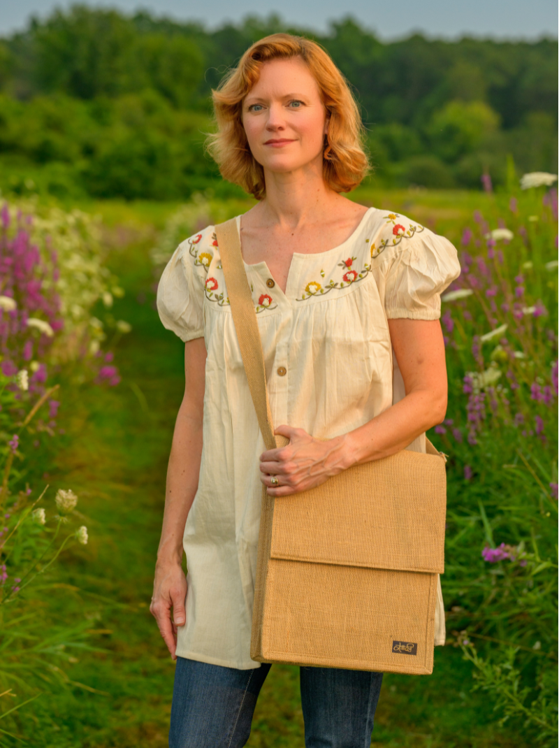 Woman holding a beige bag in a field with greenery and flowers