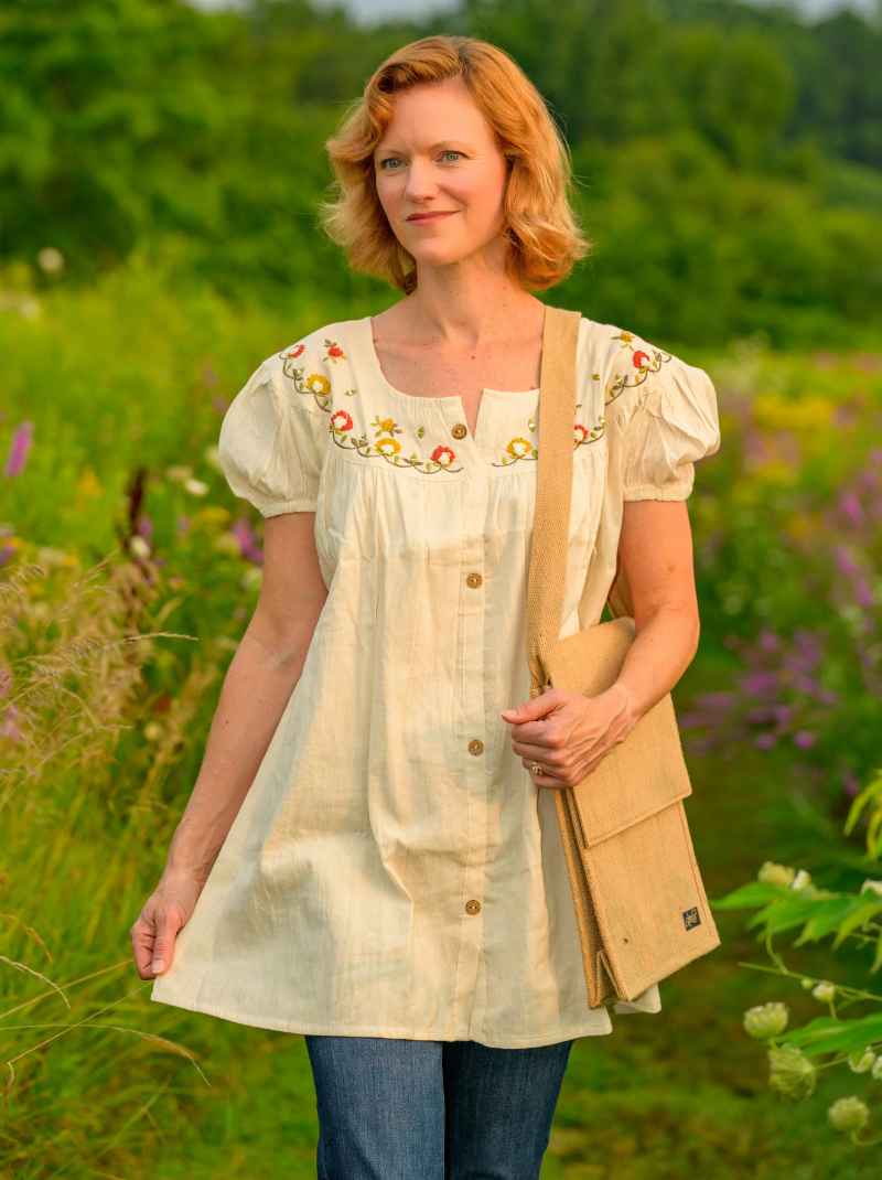 Woman in a beige embroidered blouse standing in a field with flowers