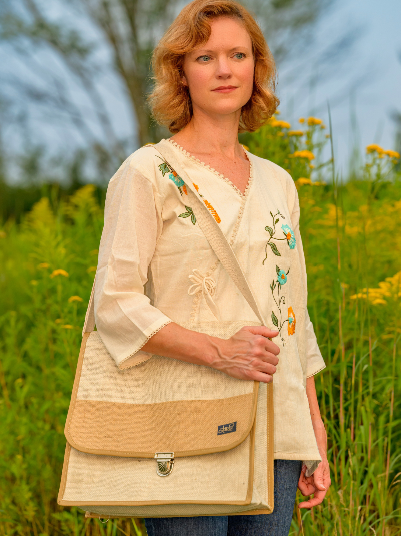 Woman holding a beige bag with floral embroidery in a grassy field
