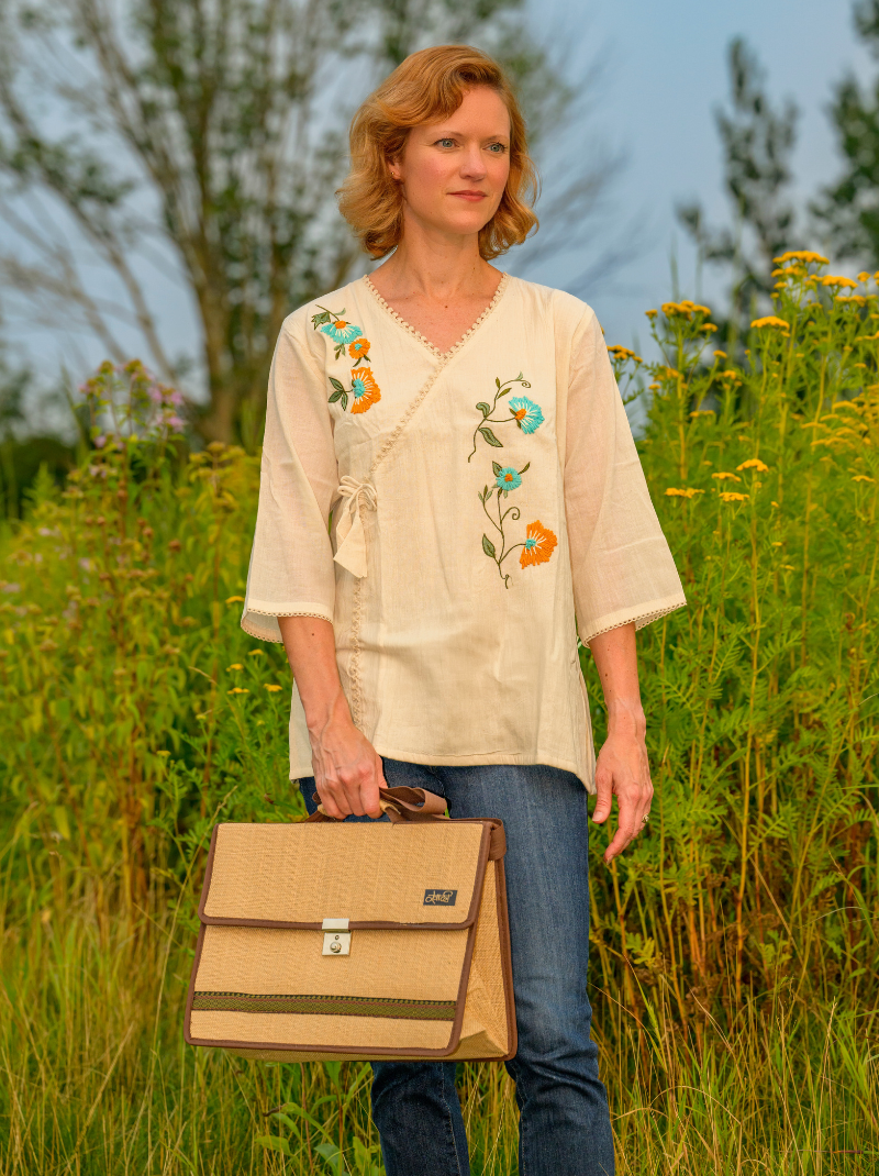 Woman holding a beige bag in a field with embroidered top