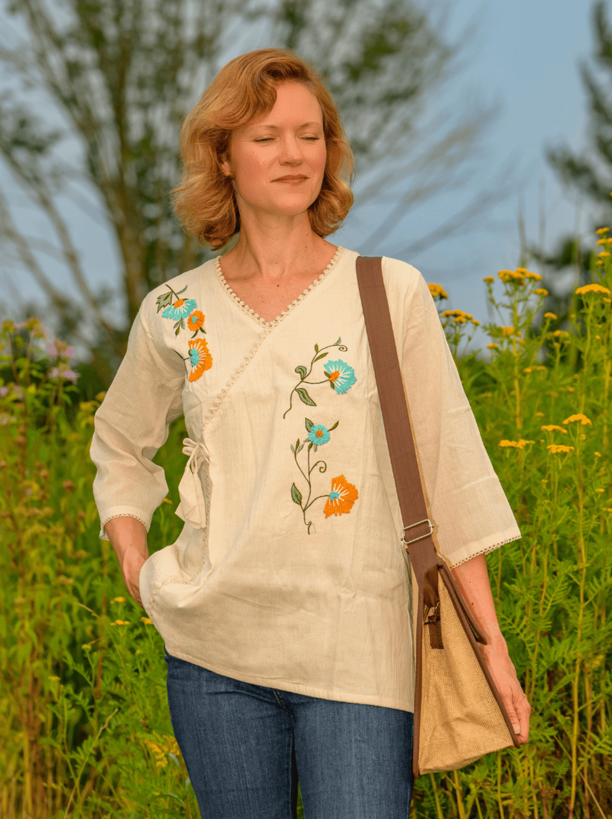 Woman wearing a cream-colored blouse with floral embroidery in a field of flowers.