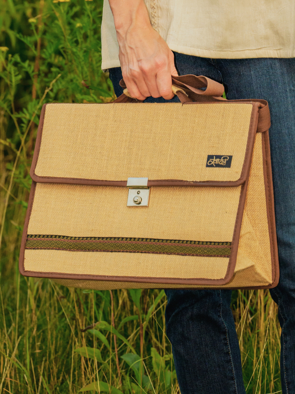 Person holding a beige and brown bag with a visible brand logo in a grassy outdoor setting