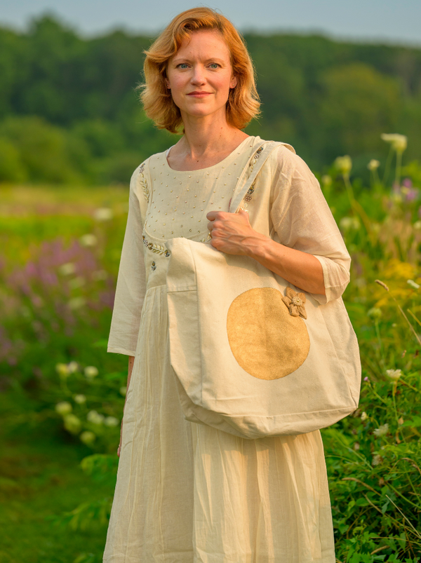 Woman holding a beige tote bag with a large brown circle in a field
