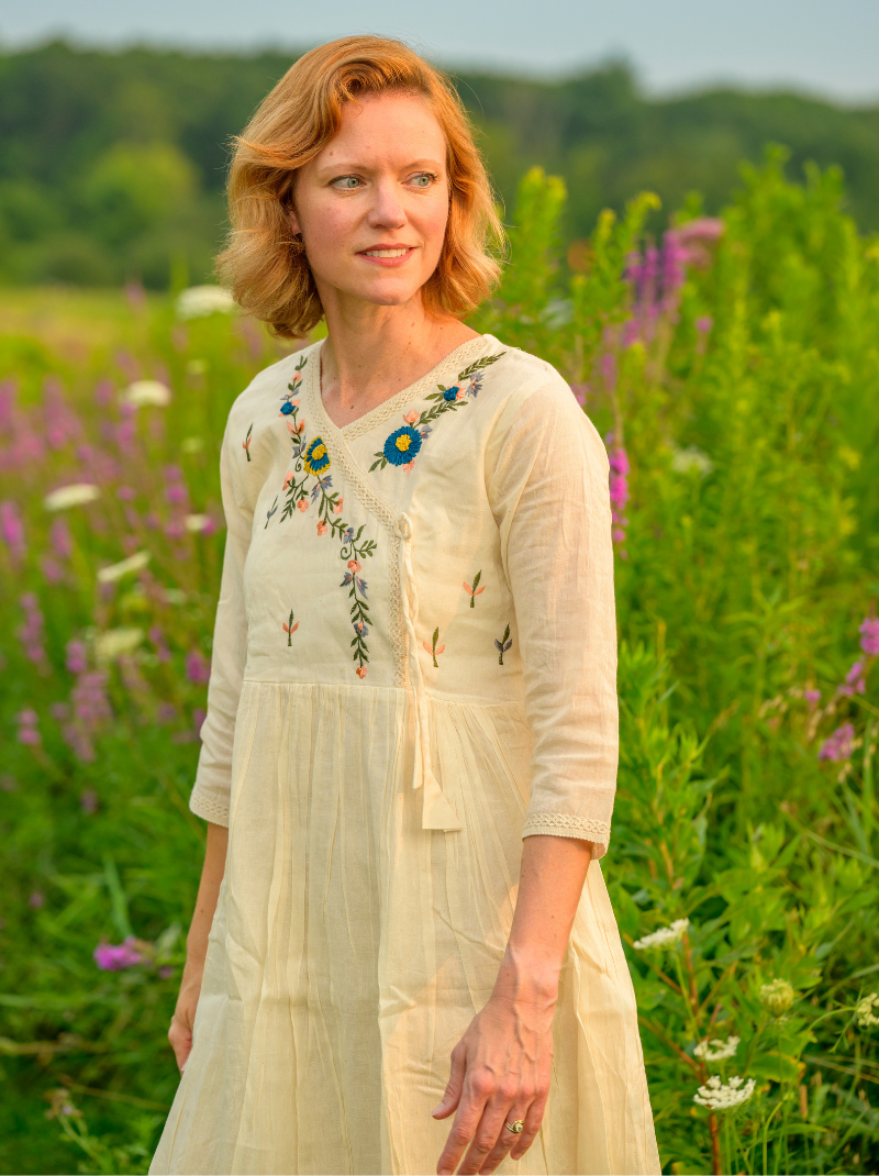 Woman in a white dress with floral embroidery standing in a field of flowers.