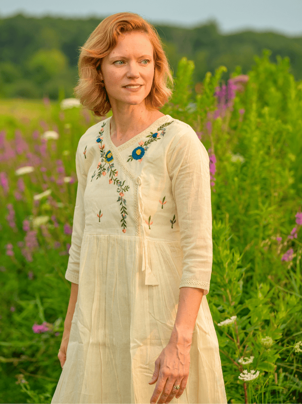 Woman in a white dress with floral embroidery standing in a field of flowers.