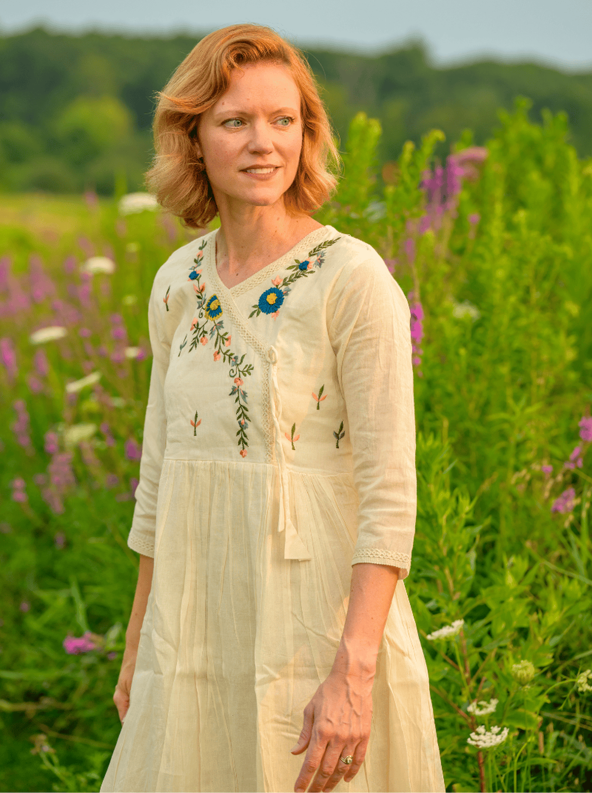 Woman in a white dress with floral embroidery standing in a field of flowers.