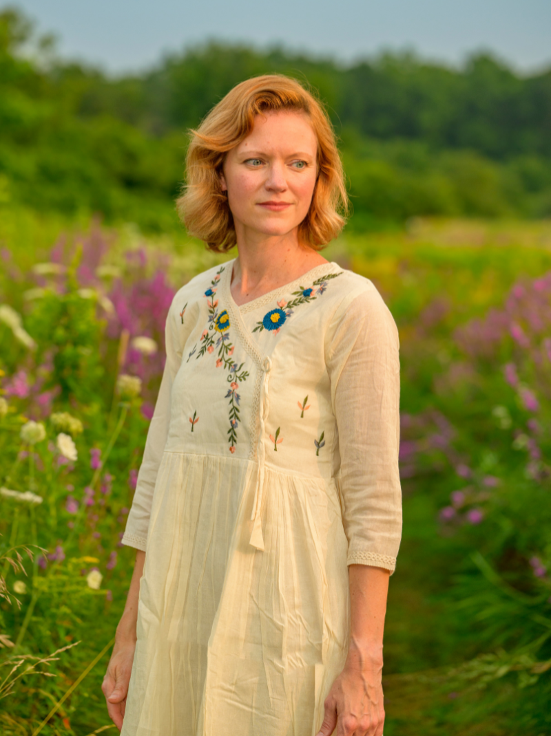 Woman in a light dress with floral embroidery standing in a field of flowers.
