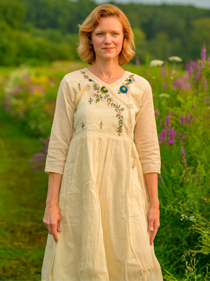 Woman in a white dress with floral embroidery standing in a field of flowers.