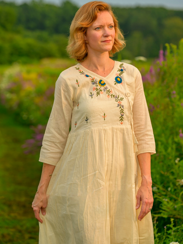 Woman wearing a cream-colored dress with floral embroidery standing in a field of flowers.