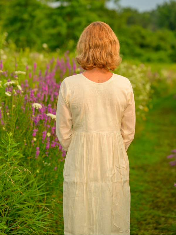Woman in a white dress standing in a field of purple flowers and green grass.