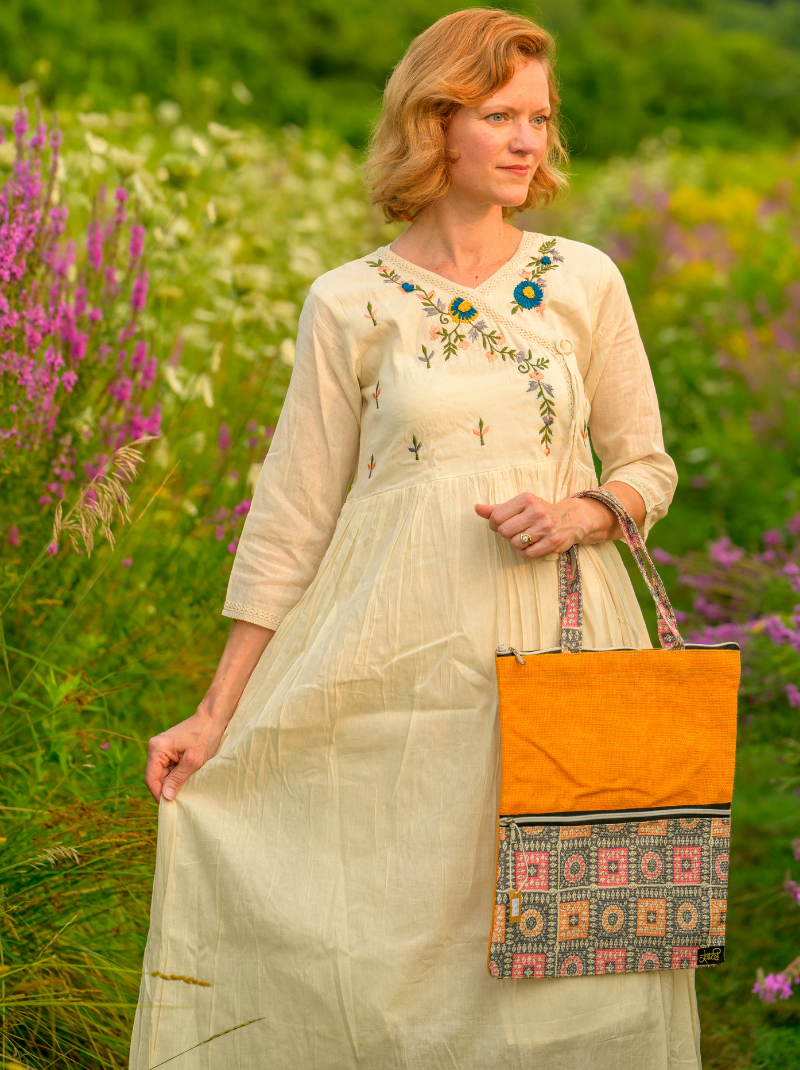 Woman in a light dress holding an orange bag with floral patterns in a field of flowers.