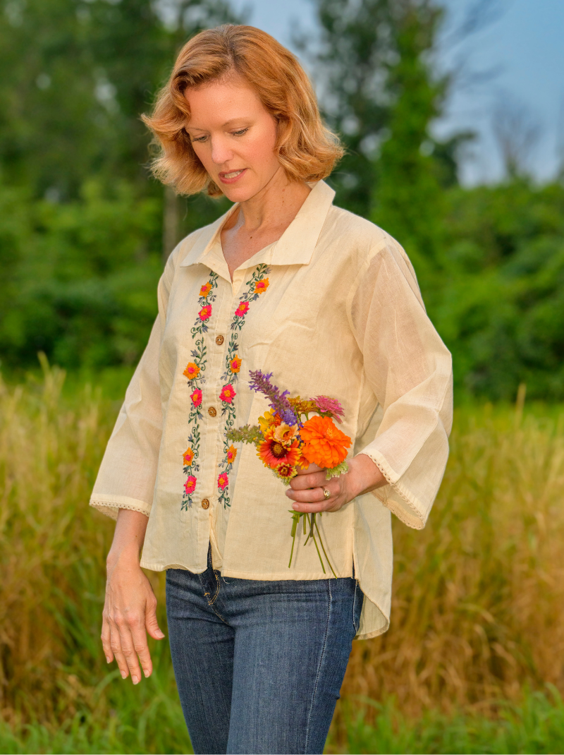 Woman in a beige shirt with floral embroidery holding flowers in a field