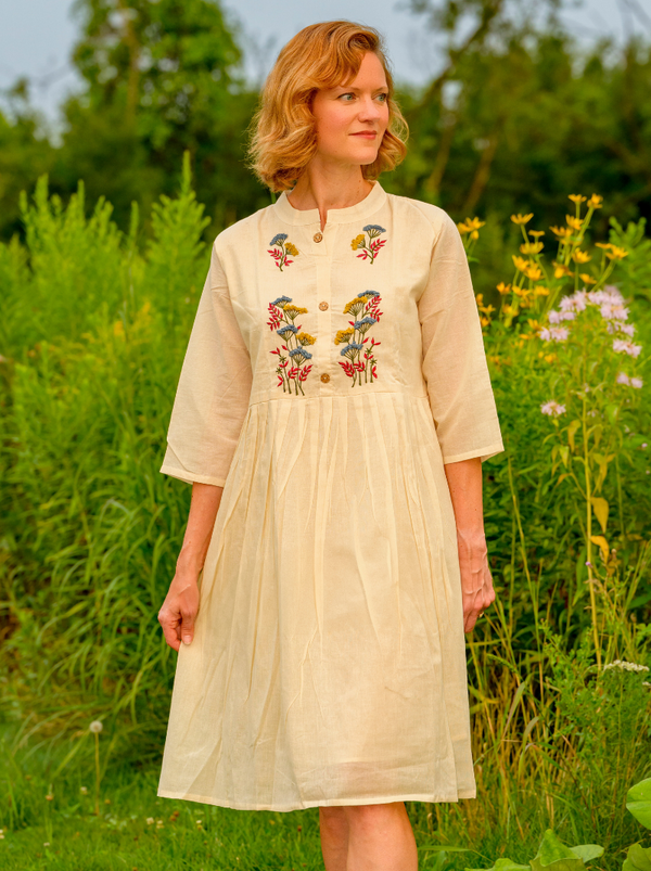 Woman wearing a beige dress with floral embroidery in a natural setting