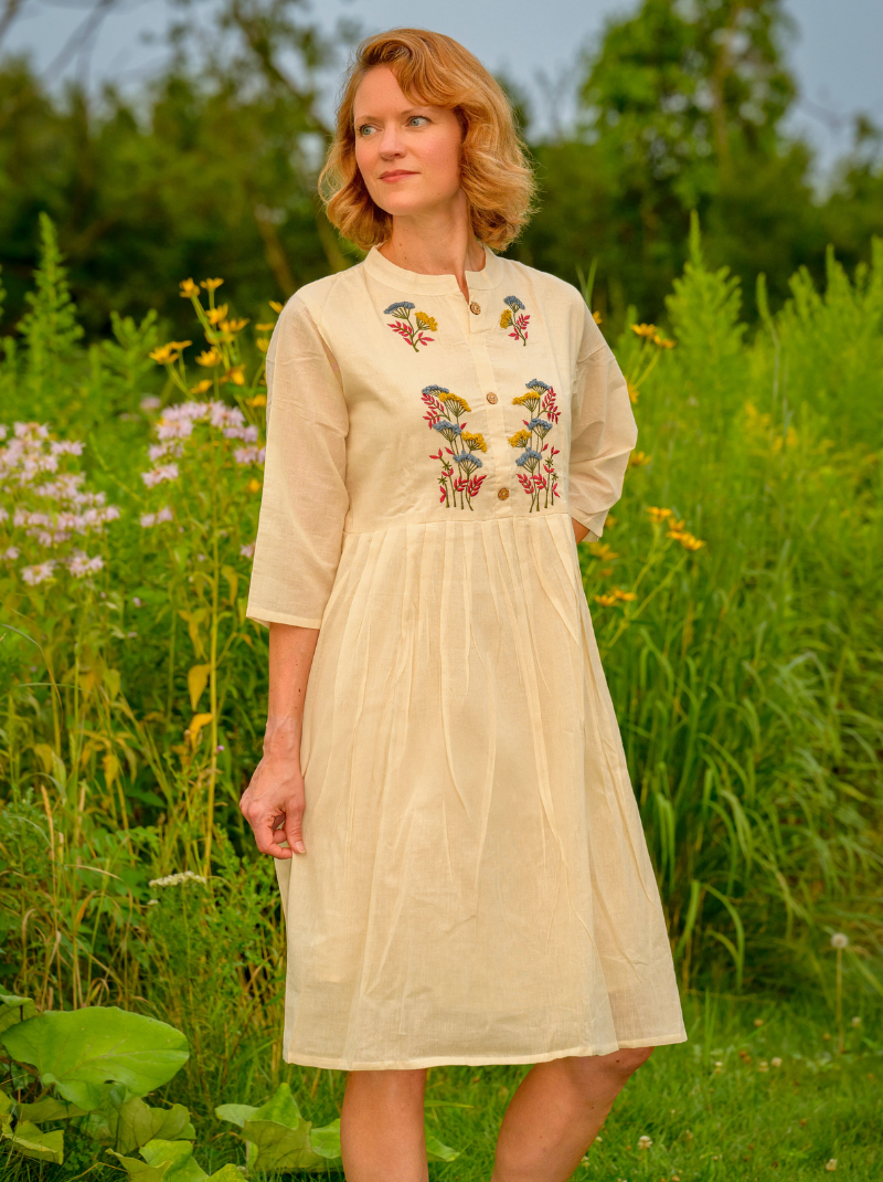 Woman wearing a beige dress with floral embroidery in a natural setting