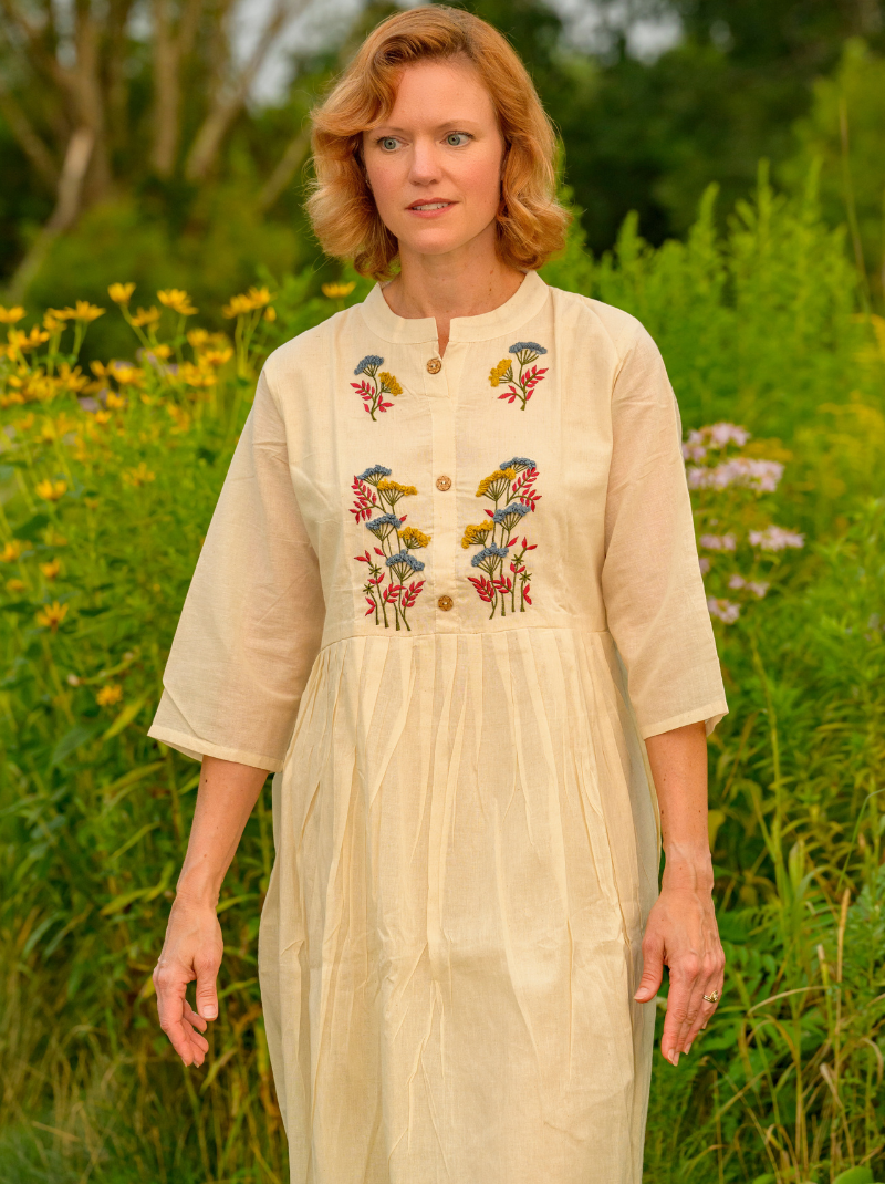 Woman wearing a beige dress with floral embroidery in a natural setting