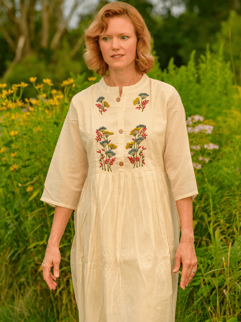 Woman wearing a beige dress with floral embroidery in a natural setting