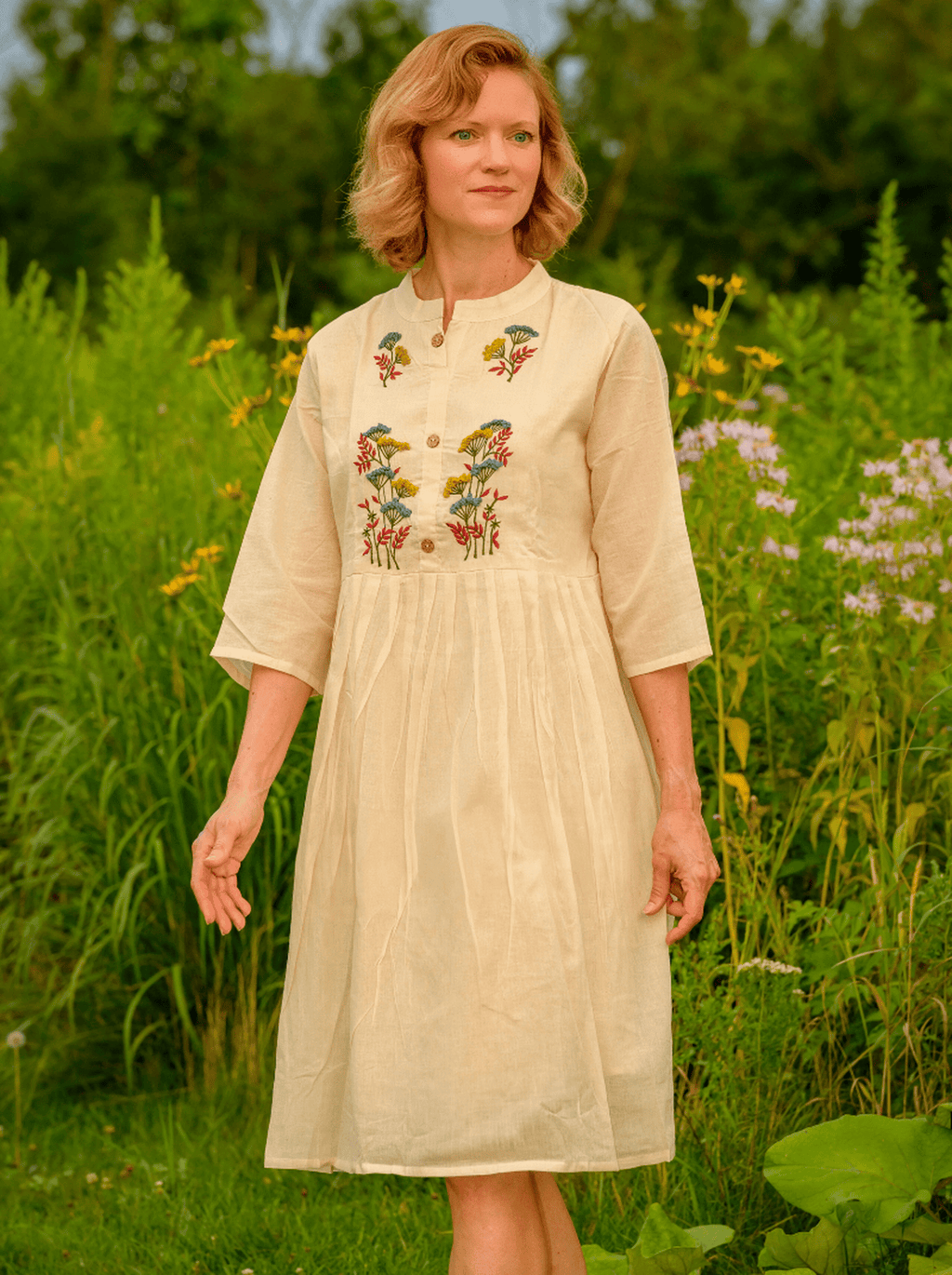 Woman wearing a beige dress with floral embroidery in a natural setting