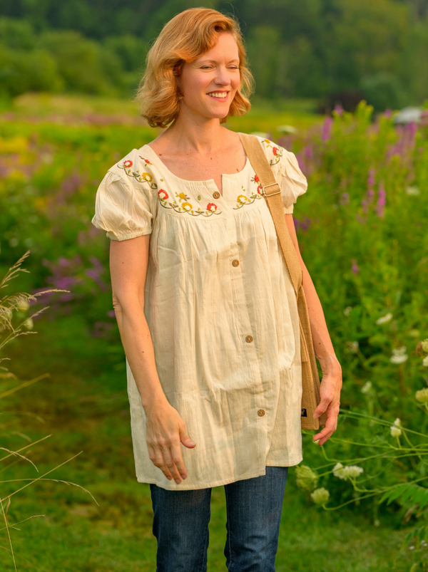 Woman wearing a light-colored dress with floral embroidery in a field of flowers