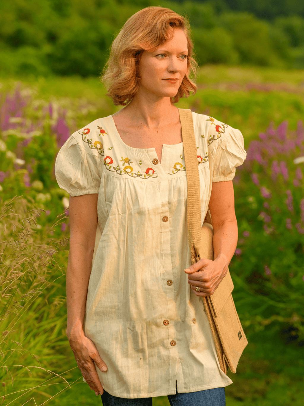 Woman in a white embroidered blouse standing in a field with flowers