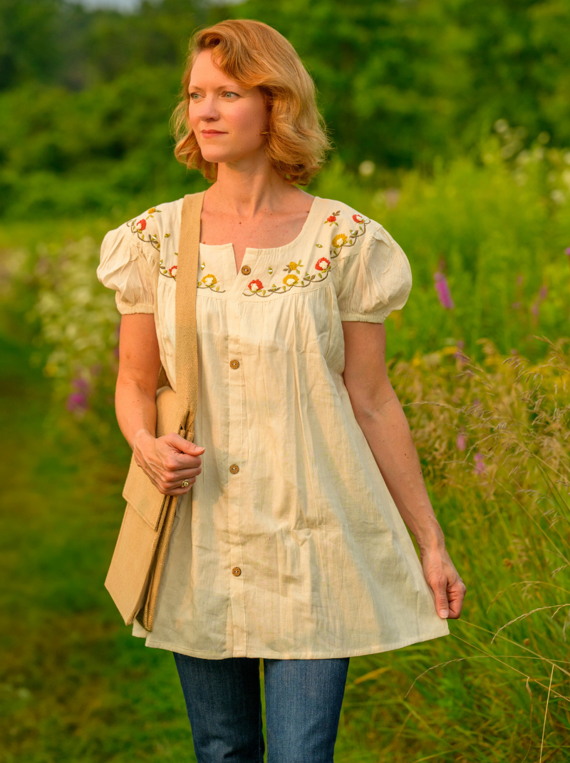 Woman wearing a light-colored embroidered dress in a natural setting