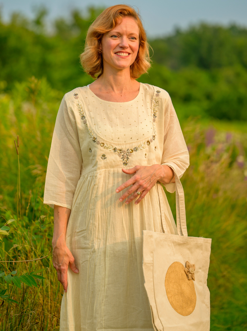 Woman in a light dress holding a tote bag with a floral pattern in a field.