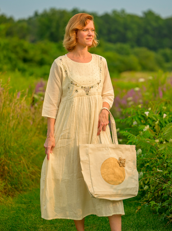 Woman in a light dress holding a tote bag with a pumpkin design in a field.