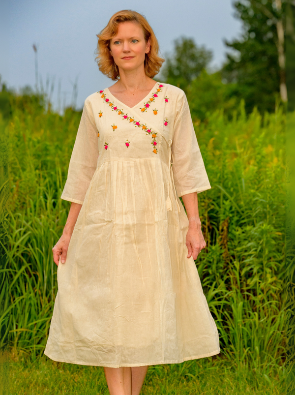 Woman wearing a beige dress with floral embroidery in a grassy field