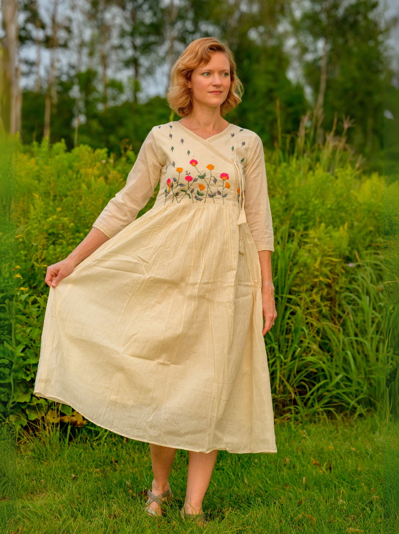 Woman wearing a beige dress with floral embroidery in a grassy field