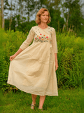 Woman wearing a beige dress with floral embroidery in a grassy field