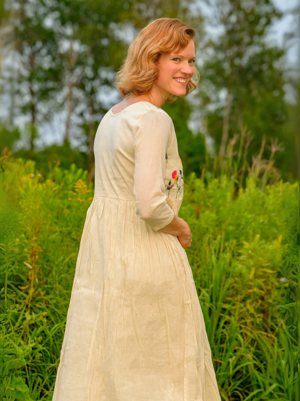 Woman in a white dress standing in a natural setting with trees and greenery.