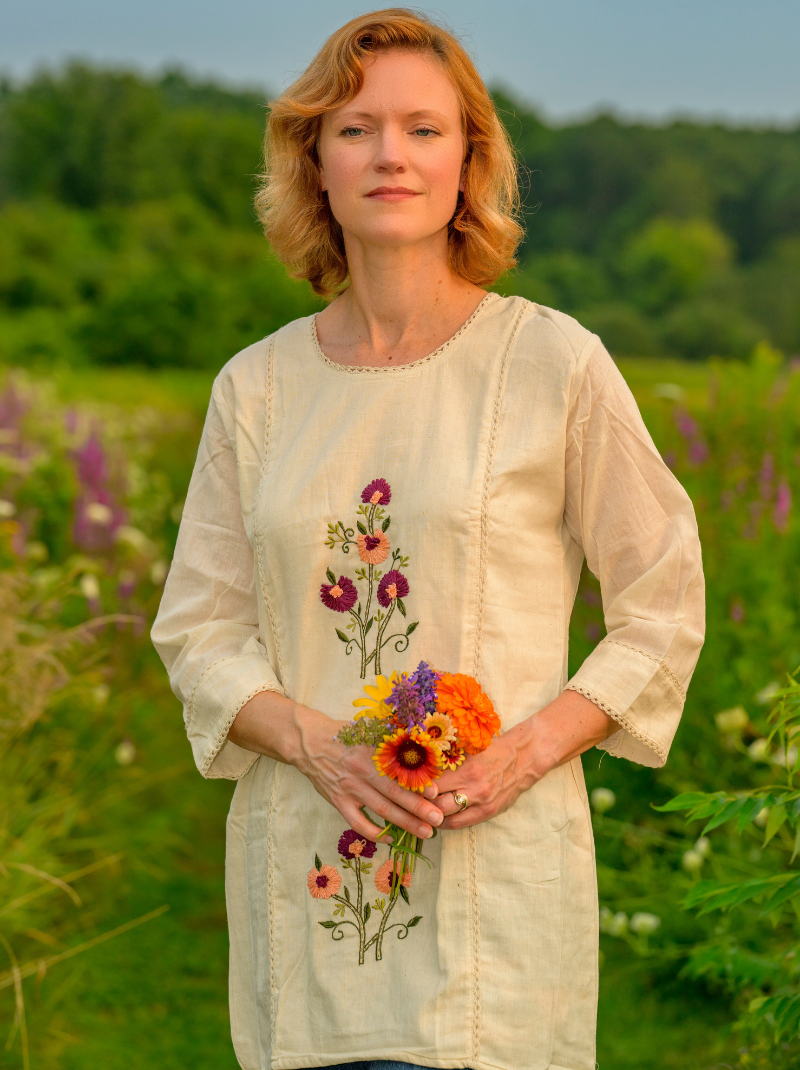 Woman holding flowers in a field with a floral embroidered shirt