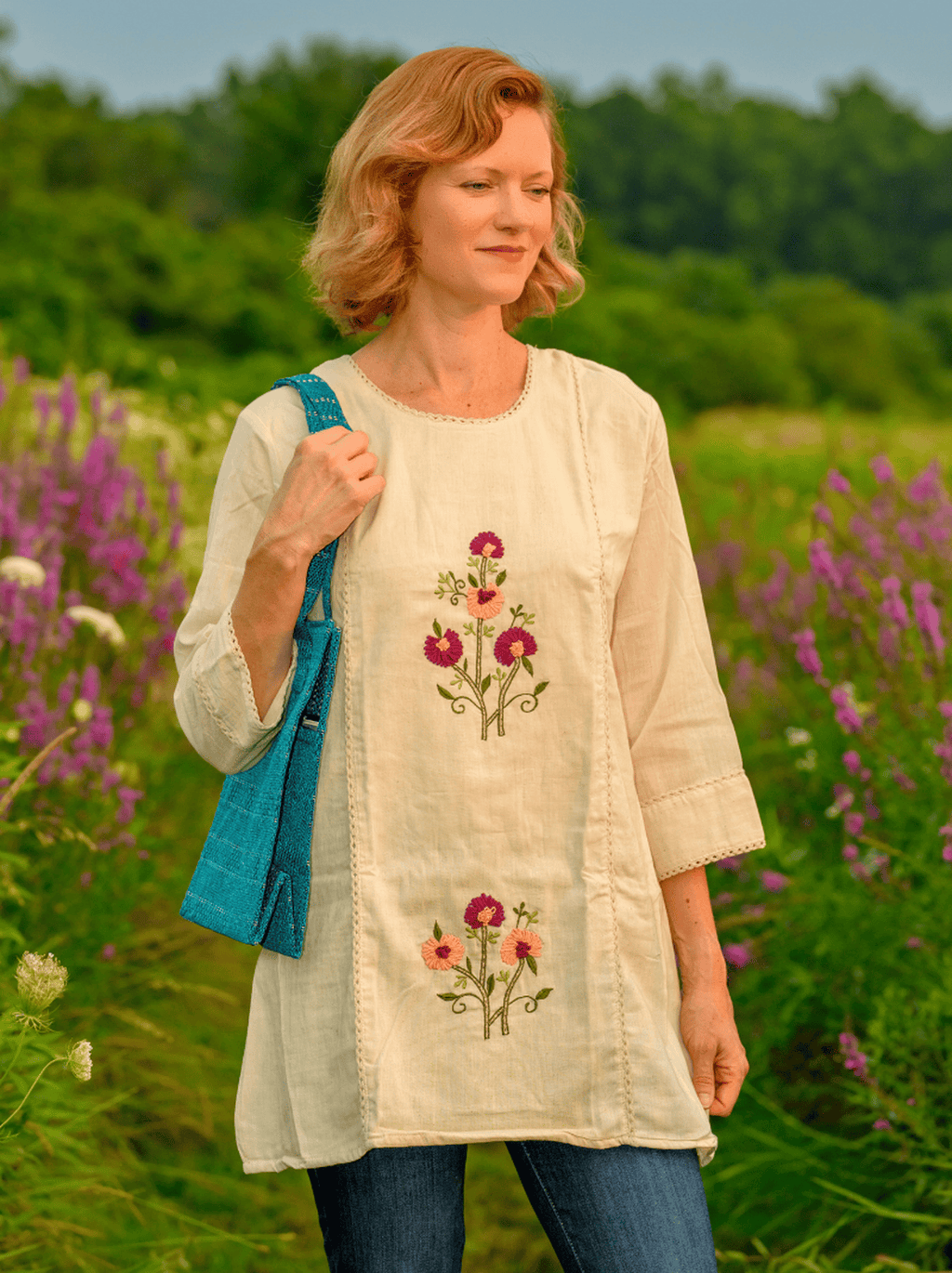 Woman wearing a light-colored dress with floral embroidery in a field of flowers.