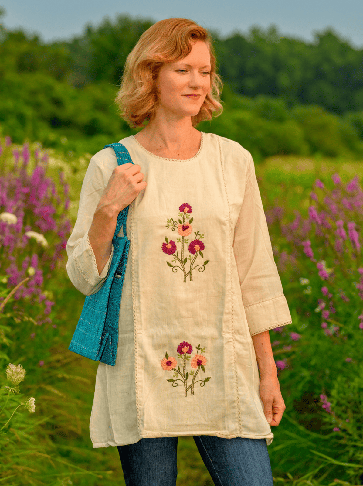 Woman wearing a light-colored dress with floral embroidery in a field of flowers.