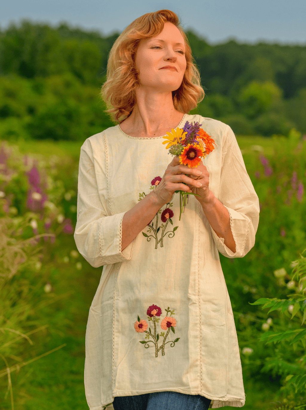 Woman holding a bouquet of flowers in a field with embroidered shirt