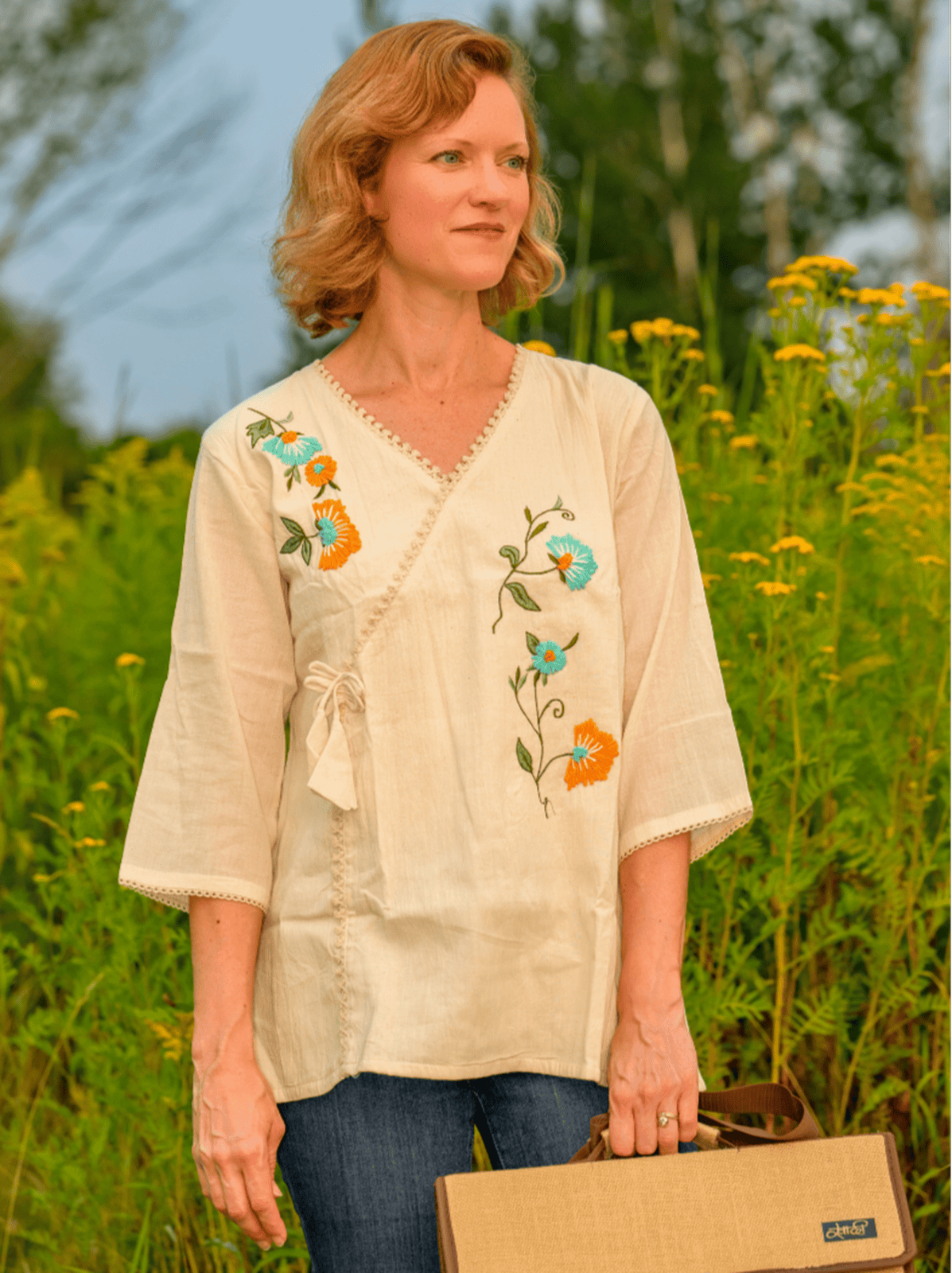 Woman wearing a beige embroidered blouse standing in a field with flowers.