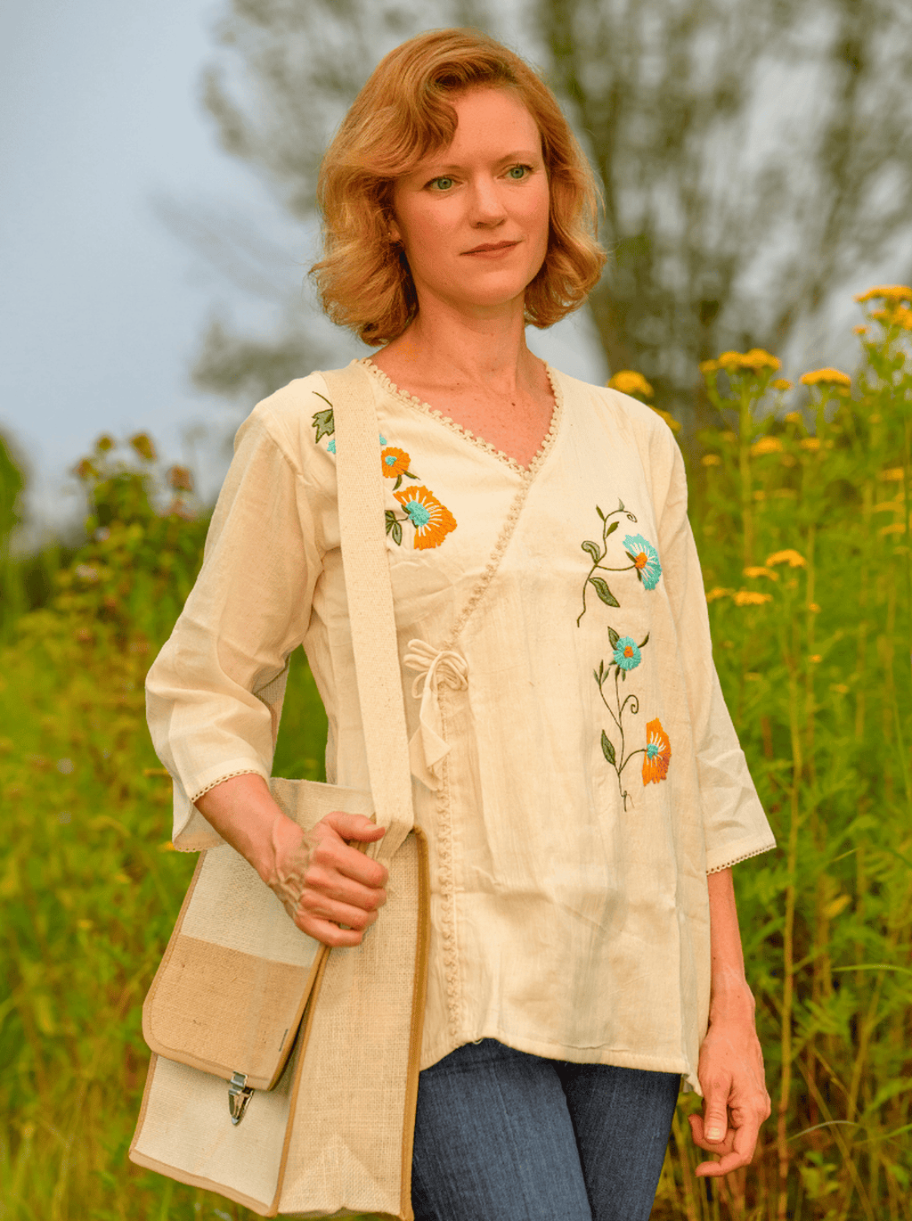 Woman wearing a beige embroidered blouse standing in a field with wildflowers.